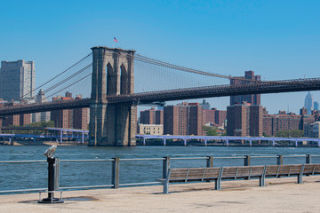 Fototapeta premium Sunny day view of Brooklyn Bridge, American flag, East River and Manhattan Skyline with blue sky