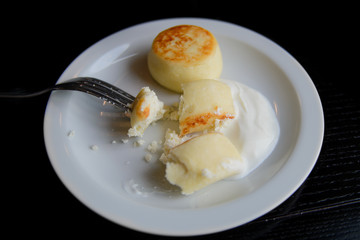 Two cheesecakes on a white plate with sour cream in the process of eating