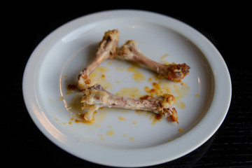 Leftovers from chicken legs on a plate on a black table