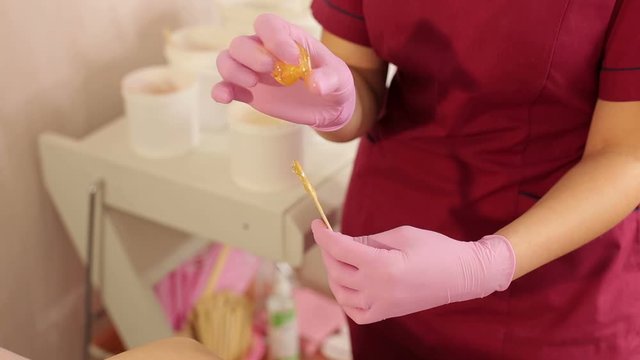 Beautician removes sugar paste for waxing with wooden stick, preparing for the sugaring of woman armpits. Beautician takes sugar paste with a spatula from the banks for depilation of the woman armpits