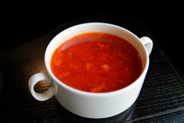 Borsch in a deep white plate on a black wooden table
