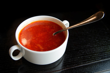 Borsch in a deep white plate on a black wooden table with a spoon