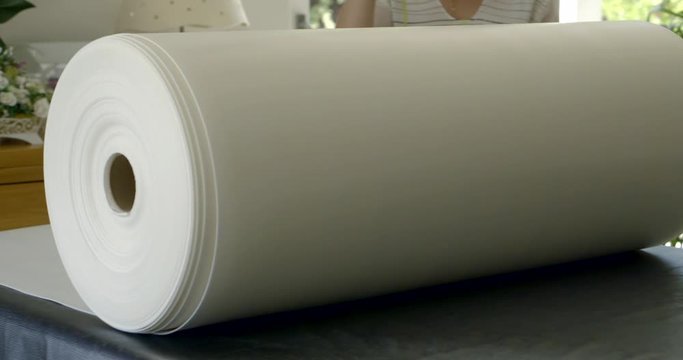 woman is unrolling large roll with white fabric on table in fabric store