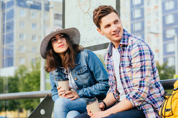 Elegant young brunette woman in hat and denim jacket and her boyfriend drinking coffee outdoor...