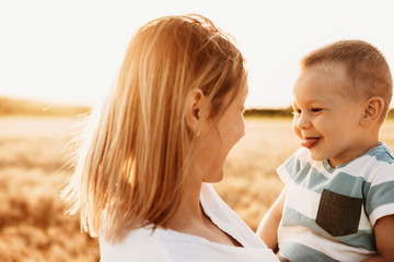 Close up portrait of cute young boy playing with his mother while showing his tongue against sunset in a wheat field.