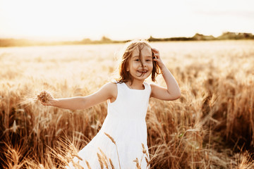 Portrait of lovely little girl playing in what field dressed in white dress looking at camera laughing.