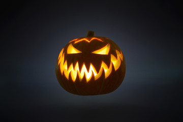 Flying bright orange Jack-o'-lantern pumpkin on dark solid background. Glowing eyes and a terrible grin. Halloween minimal concept. Copy space. Desktop wallpapers