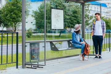 Couple communicating while waiting at bus stop. Hansome man and elegant woman with backpacks meets...