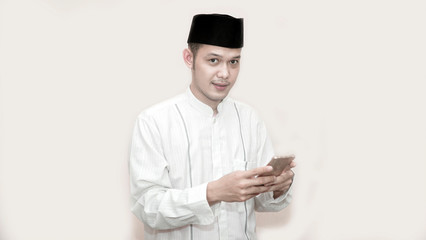 portrait of handsome asian muslim man with head cap and using smartphone taking a call and smile at camera