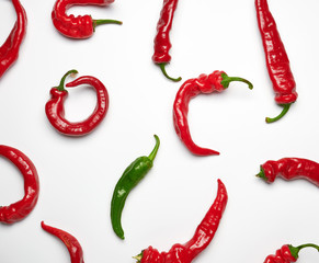 many red whole fruits of hot pepper and one green on a white background