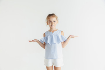 Stylish little smiling girl posing in casual clothes isolated on white studio background. Caucasian blonde female model. Human emotions, facial expression, childhood. Showing empty space, inviting