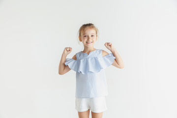 Stylish little smiling girl posing in casual clothes isolated on white studio background. Caucasian blonde female model. Human emotions, facial expression, childhood. Winning, celebrating, smiling.