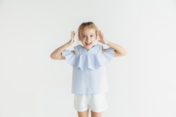 Stylish little smiling girl posing in casual clothes isolated on white studio background. Caucasian blonde female model. Human emotions, facial expression, childhood. Looks happy and amazed.