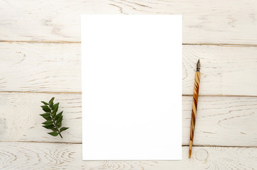 Blogger's workdesk mockup with A4 paper list and a nib pen, top view with a place for text on a white wooden background with green leaves