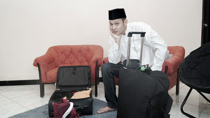 handsome muslim asian man with traditonal songkok or head cap prepare suitcase luggage for eid mubarak holiday