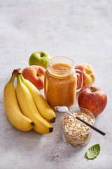 Fresh fruit smoothie made from banana, apple, peach, oat and chia. Healthy fruit beverage in a jar and ingredients on a stone background. Copy space