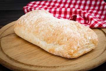 Loaf of ciabatta bread on a cutting board on the dark wooden table