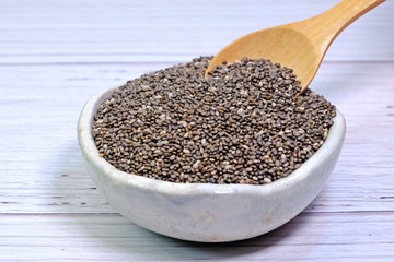 Little wooden spoon picking Chia seeds from small white ceramic bowl.