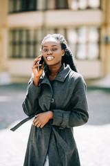 Portrait of young african american girl talking by mobile phone, smiling. Sunny day. Outdoor photo.