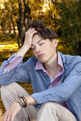 Stylish Young man outdoors sits near a pond with a sad face. Love feelings, immersed in emotions, autumn season.