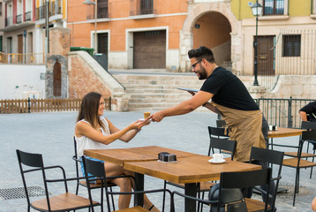 Fototapeta na wymiar A waiter is serving a coffee to a young woman on a pub terrace