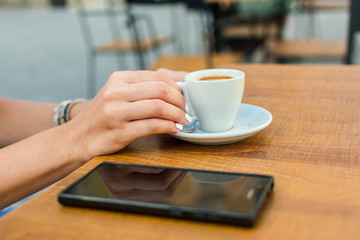 Hands of a young woman are holding a cup of coffee on a terrace of a pub