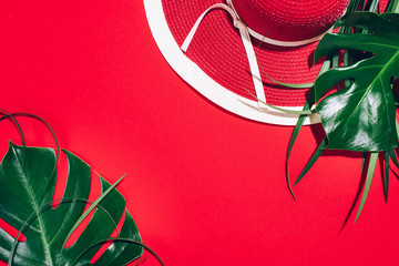 Women's summer red hat, tropical palm and monstera leaves on paper background with copy space. Top view, flat lay. Summer travel and holiday concept