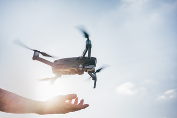 Man using a drone with remote controller. Close up hand with landing quadcopter. Silhouette.