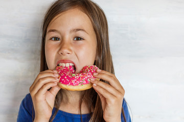 A beautiful little girl is eating a pink donut. Sweet treat