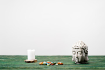 buddha statuette, candle and colorful semiprecious stones on wooden surface isolated on white