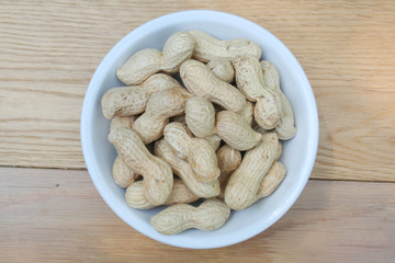 Peanuts in nutshell in a bowl on wooden table