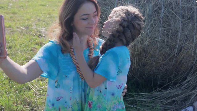 Mom photographs the kiss of a child on a mobile. A field with straw bales.
