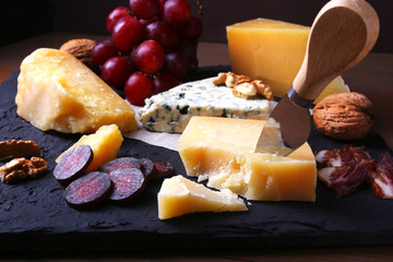 Assortment of cheese with fruits, grapes, nuts and cheese knife on a wooden serving tray.