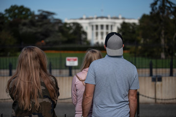 Three people standing in front of the blurred grided White house in Washington, DC. Back view. Concept photo.