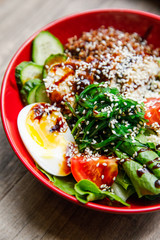 delicious and appetizing salad egg, tomato, spinach, cucumber, cheese, cilantro, lies on a red plate in a restaurant