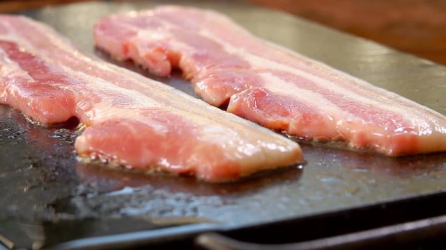 Two strips of raw bacon are roasted on the hot stone surface of the grill