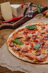 italian pizza with assorted sausages and hot pepper, the background is decorated with vegetables, on a wooden background