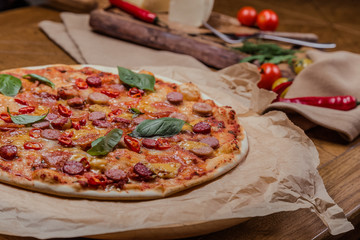 italian pizza with assorted sausages and hot pepper, the background is decorated with vegetables, on a wooden background