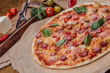 italian pizza with assorted sausages and hot pepper, the background is decorated with vegetables, on a wooden background