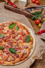 italian pizza with assorted sausages and hot pepper, the background is decorated with vegetables, on a wooden background