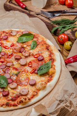 italian pizza with assorted sausages and hot pepper, the background is decorated with vegetables, on a wooden background