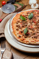 Pizza Bolognese with basil on a wooden board, background wooden decorated with vegetables and cutlery