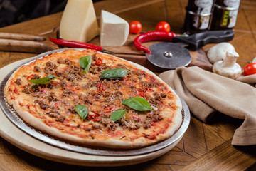 Pizza Bolognese with basil on a wooden board, background wooden decorated with vegetables and cutlery