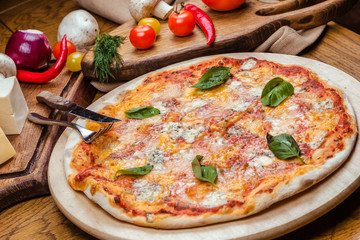 Pizza four cheeses with basil on a wooden board, wooden background decorated with vegetables and cutlery