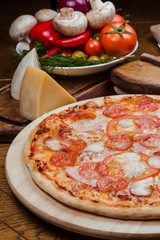 salami pizza on a wooden board, wooden background decorated with vegetables and cutlery