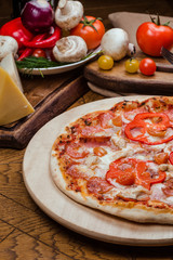 salami pizza on a wooden board, wooden background decorated with vegetables and cutlery