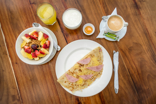 Breakfast based on fresh fruits such as strawberry, melon, orange, apple and cereal, orange juice, yogurt, a posillo of honey, a coffee with milk and a plate with a large stuffed omelet