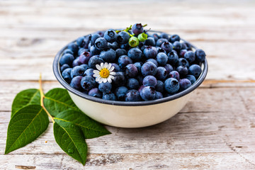 Freshly picked ripe blueberries in a bowl on a wooden background. 