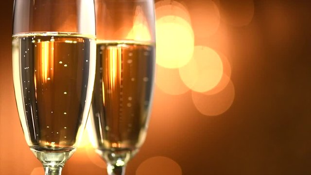 Champagne. Two flutes with sparkling wine over golden holiday background. Celebration. Slow motion 4K UHD video footage. 3840X2160