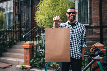 Bearded male courier with bicycle delivery food service at home. Shopping paper bag with copy space for your text or advertising content. No name shopping bag